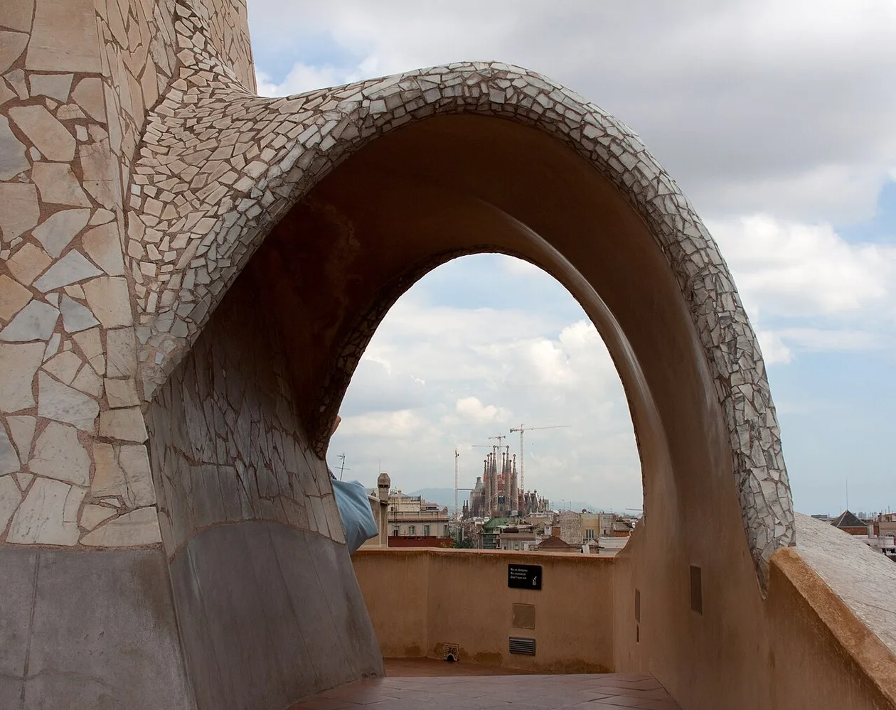 White trencadís arch on the Casa Milà rooftop framing the Sagrada Família in the distance