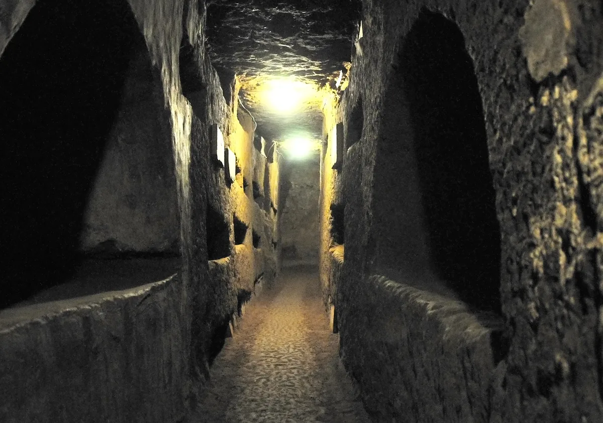 A lamp-lit burial gallery in the Catacombs of Domitilla, niches cut into the tufa on both sides