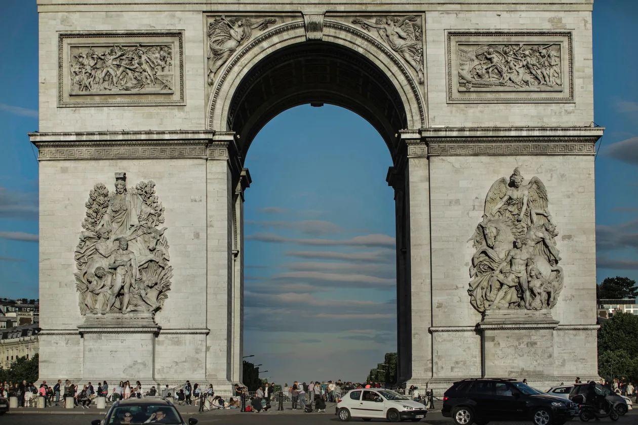 The Arc de Triomphe seen head-on from the Champs-Élysées, both sculpted groups on the east façade in afternoon light