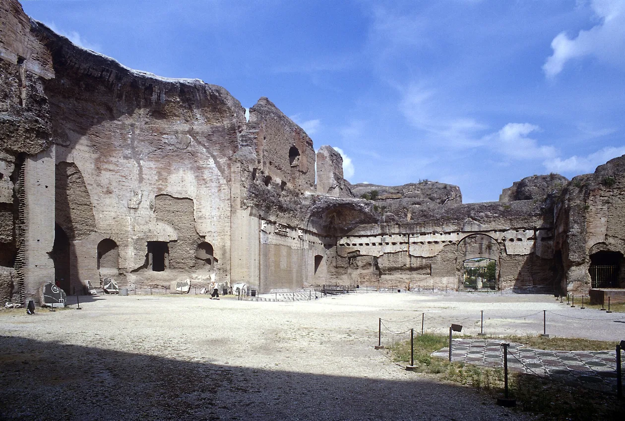 The south-east palaestra of the Baths of Caracalla, its walls standing several storeys high around an open gravel court, with a black-and-white mosaic pavement in the foreground