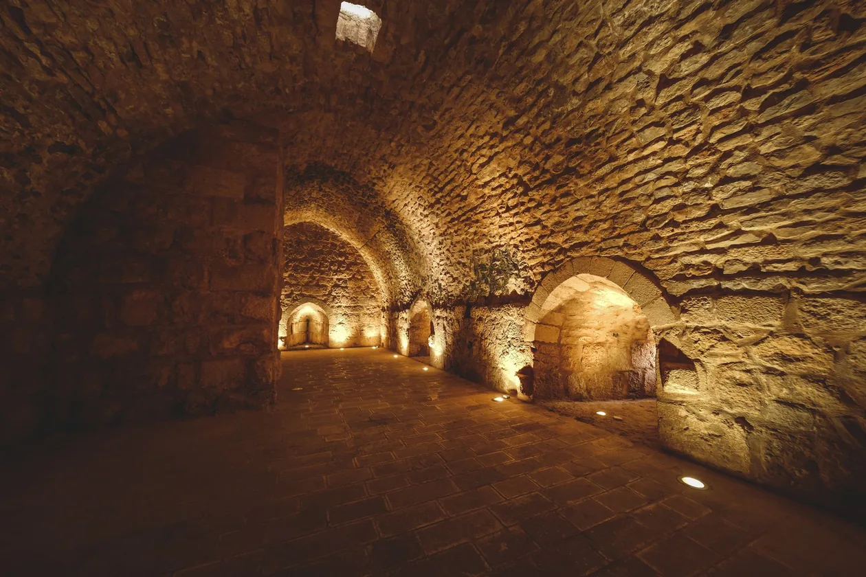 Warm light along an ancient underground stone gallery lined with arched recesses