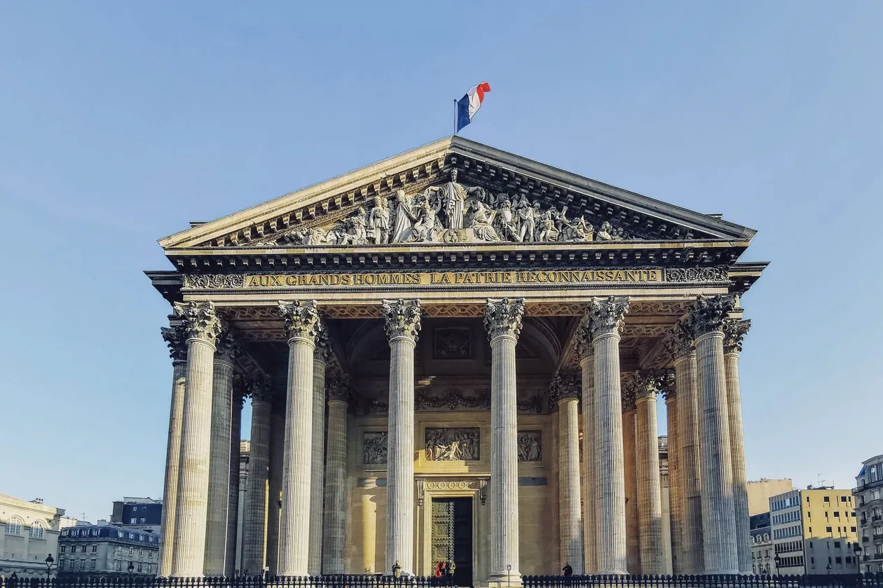 The neoclassical portico of the Panthéon in Paris seen head-on, Corinthian columns under the pediment inscribed Aux grands hommes la patrie reconnaissante, with the French flag above