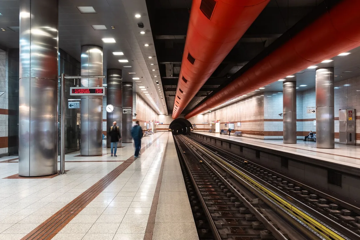 Platform of a modern Athens metro station with its red ceiling ducts and steel columns