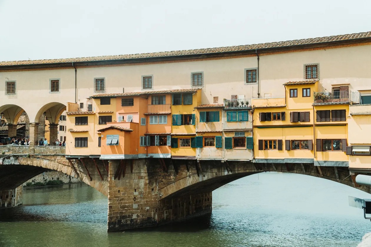 The Ponte Vecchio from the riverbank, the goldsmiths' shops hanging over the Arno and, running along the top of the bridge, the continuous cream-coloured upper storey with small square windows that carries the Vasari Corridor